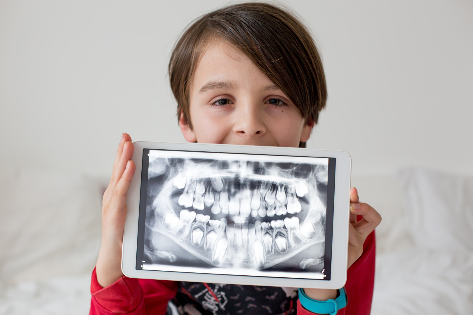 Child holding a tablet showing dental x-ray images at periodontist office